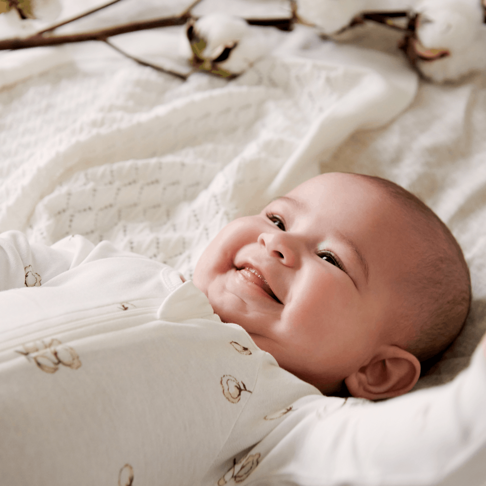Baby lying on a white textured blanket with cotton flowers in the background