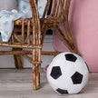 Plush soccer ball on a wooden floor with a chair and pink cushion in the background