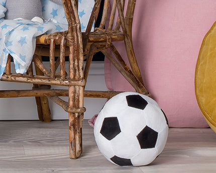 Plush soccer ball on a wooden floor with a chair and pink cushion in the background