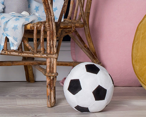 Plush soccer ball on a wooden floor with a chair and pink cushion in the background