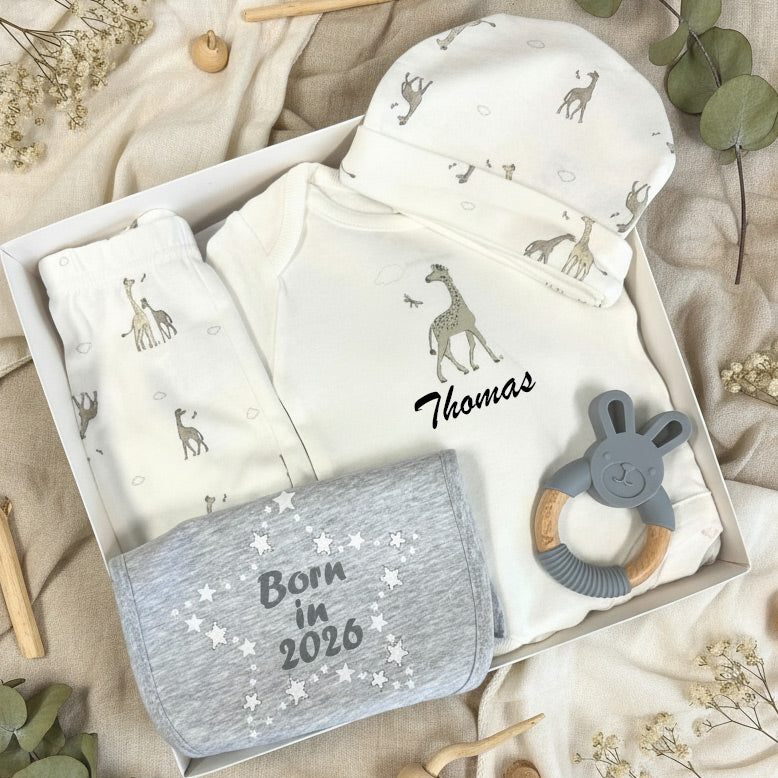 Gift box with giraffe baby clothes on a natural fabric background
