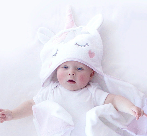 Baby wearing a white hooded towel with unicorn face design on a white background