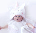 Baby wearing a white hooded towel with unicorn face design on a white background