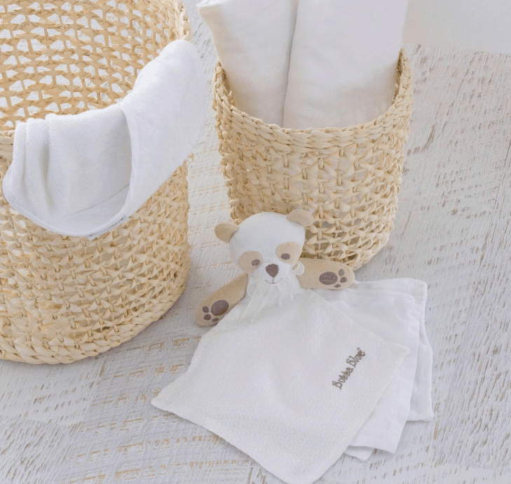 Baby items including a white blanket, baby booties, and a plush toy on a textured surface.