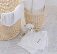 Baby items including a white blanket, baby booties, and a plush toy on a textured surface.