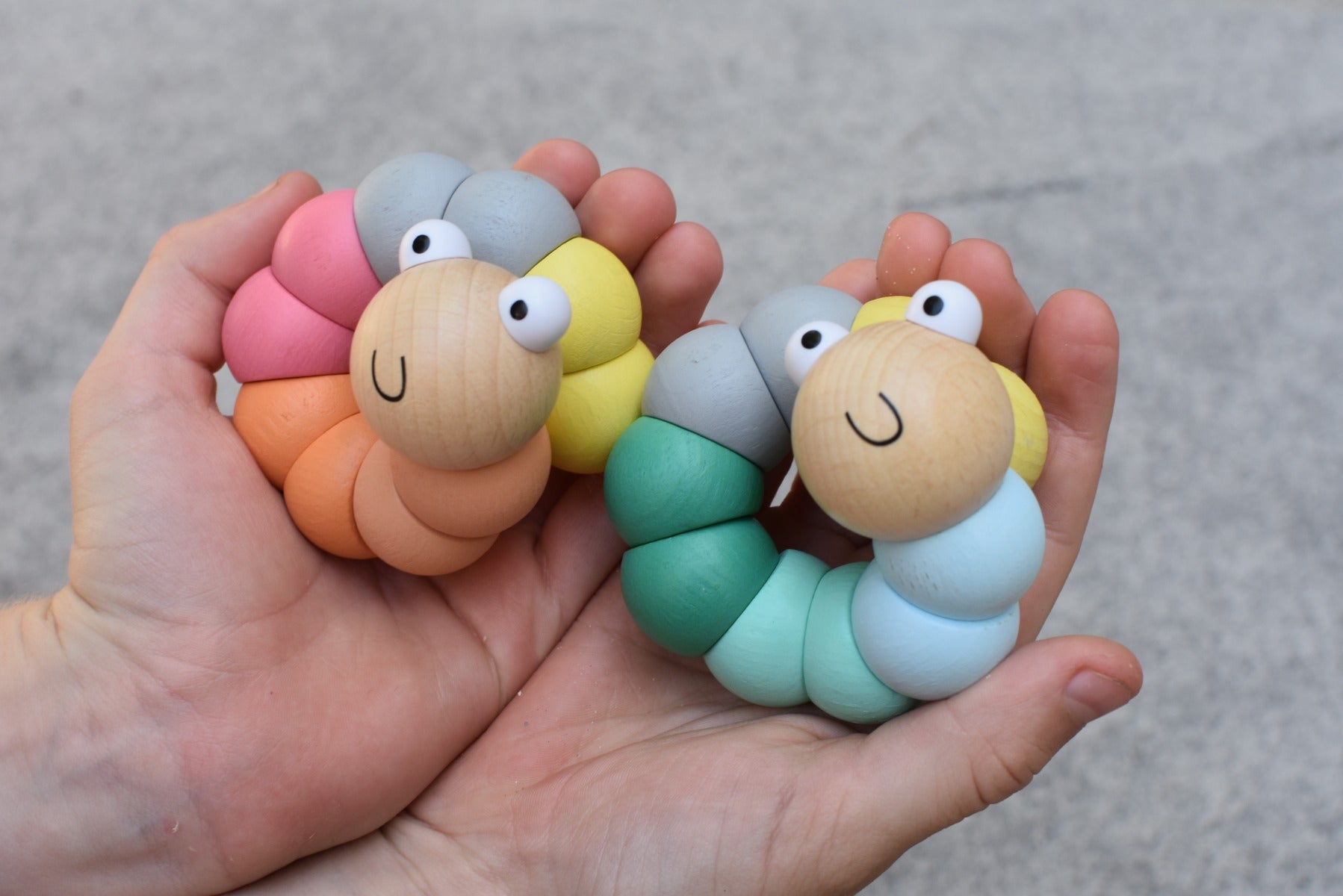 Colorful caterpillar-shaped toys held in a hand against a neutral background
