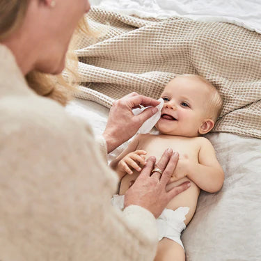 Baby lying on a bed with a person applying cream or lotion to their skin.